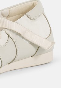 Lys beige lærstøvel med en glatt overflate, utstyrt med et teksturert stoffbånd og en lav, flat såle. Rundt tådesign med subtile detaljer.