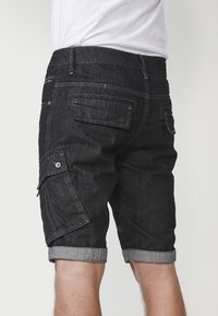 Dunkelblaue Jeansshorts mit geradem Schnitt, umgeschlagenen Säumen, mehreren Taschen und gelben Nähakzenten. Der Bund ist schlicht ohne Verzierungen.