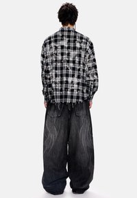 Μαύρο και άσπρο καρό υπερμεγέθες σακάκι, με ξεφτισμένο τελείωμα, συνδυασμένο με φαρδιά σκουρόχρωμα τζιν παντελόνια με κεντημένες λεπτομέρειες.