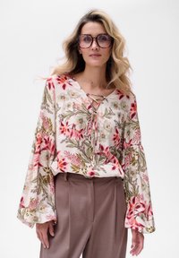 Blumenbluse aus leichtem Stoff, mit einem V-Ausschnitt und Schnürdetail, Glockenärmeln und floralen Mustern in Rosa, Grün und Beige.