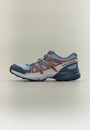 Grauer und dunkelblauer Salomon Trailrunning-Schuh mit orangefarbenen Akzenten und weißen Schnürsenkeln auf neutralem Hintergrund, Seitenansicht zeigt das Profil der Sohle.