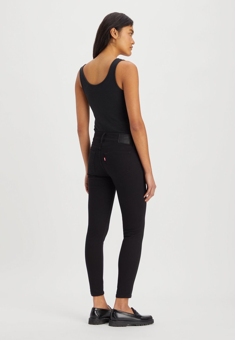 Schwarzes geripptes Tanktop, hochgeschnittene schwarze Jeans und schwarze Loafers. Glatte Textur mit enger Passform und minimalen Markenakzenten.