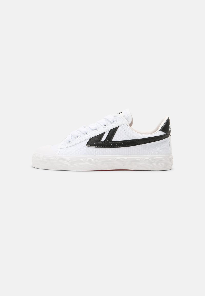 Hvit lerret sneakers med svarte accenter, rund tå og teksturert gummisåle. Har en fremtredende svart stripe på siden.