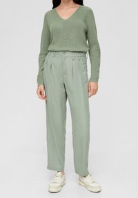 Maglione a coste verde chiaro con scollatura a V e maniche lunghe, abbinato a pantaloni plissettati verde chiaro e scarpe da ginnastica bianche.