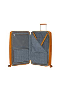 Valigia rigida arancione con un interno a motivo geometrico grigio, diversi scomparti, tasche con zip e manico retrattile in cima.