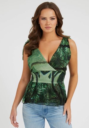 Top verde avvolgente con scollatura a V, in tessuto con motivo a foglia, vita a peplo e sovrapposizione trasparente. Abbinato a jeans azzurri chiari.