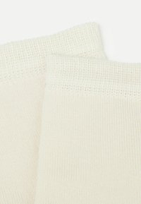 Lyst beige strikkede sokker med en glat overflade og ribbet kant, der har et jævnt mønster over det hele og ingen synlig branding.