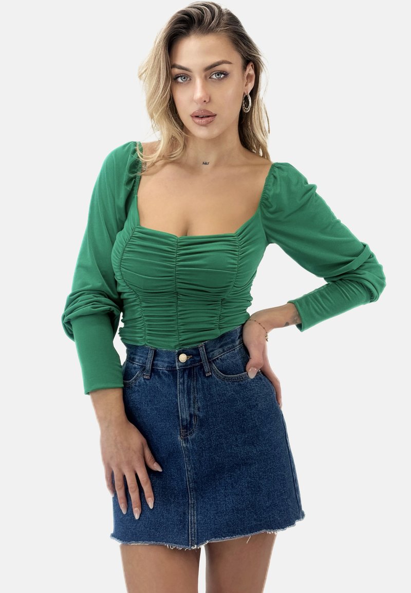 Top verde a maniche lunghe con dettagli arricciati e scollatura quadrata, abbinato a una minigonna in denim con orlo a taglio vivo e chiusura con bottoni.