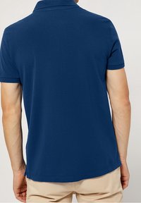 Tmavě modré polo tričko s klasickým límečkem, krátkými rukávy a texturovanou tkaninou. Má rovný lem a minimální designové detaily.