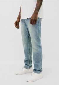 Jeans de mezclilla azul claro con corte recto, con ligeros desgastes y un sutil desvanecimiento, combinados con zapatillas blancas.