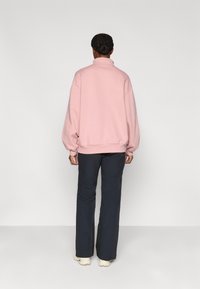 Ροζ oversized πουλόβερ με ψηλό γιακά, ριμπ μανσέτες και τελείωμα. Συνδυασμένο με σκούρο, φαρδύ παντελόνι και ανοιχτόχρωμα παπούτσια.