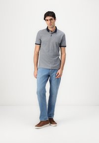 Sivi polo majica kratkih rukava s mornarskom ovratnikom i akcentima, u kombinaciji sa svijetloplavim trapericama i smeškim patikama, stoji oduzeta na bijeloj pozadini.