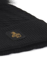 Berretto nero in maglia con texture a coste, dotato di un evidente patch con logo di forma quadrata. Il materiale sembra morbido e caldo, adatto per il freddo.