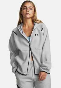 Šviesiai pilka zip-up gobtuvėlė su juodu logotipu, su gobtuvu, šoninėmis kišenėmis ir juodais akcentais siūlėse. Minkšta audinio tekstūra.