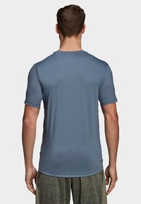 Szara koszulka sportowa, z krótkim rękawem, gładka w dotyku, dopasowany krój, tkanina odprowadzająca wilgoć, pokazana z tyłu na neutralnym tle.