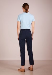 Ljusblå polo, marinblå byxor och tanfärgade slip-on skor. Byxorna har en skräddarsydd passform med bakfickor och detaljer i guldton.