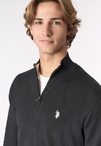 Maglione zip-neck nero realizzato in tessuto lavorato a maglia, con un piccolo logo bianco sul lato sinistro del petto e un colletto a costine per aggiungere texture.