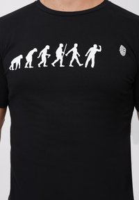 Black t-shirt featuring white graphic of human evolution from ape to modern human, with a round logo detail on the right side.