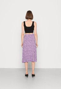 Top cropped preto combinado com uma saia midi roxa com padrão floral em preto, apresentando uma textura suave e uma bainha reta.