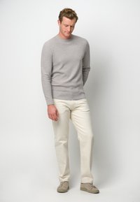 Hellgrauer Strickpullover mit Rundhalsausschnitt, kombiniert mit kremfarbenen Hosen und grauen Sneakers. Einfaches und figurnahes Design.