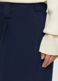Hosen in Marineblau mit glatter Textur und taillierter Passform. Verfügt über eine seitliche Tasche und ein dezentes Markenetikett in der Nähe des Bundes.