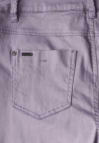 Shorts in tessuto lilla con una caratteristica tasca posteriore a forma punta, accentuata da un bottone argentato e dettagli ricamati sottili.