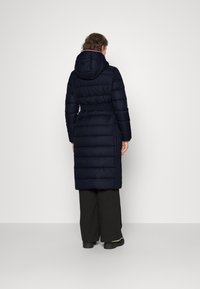 Manteau rembourré bleu marine, longueur genoux, avec capuche et taille ceinturée, présentant un design matelassé et des manches longues.