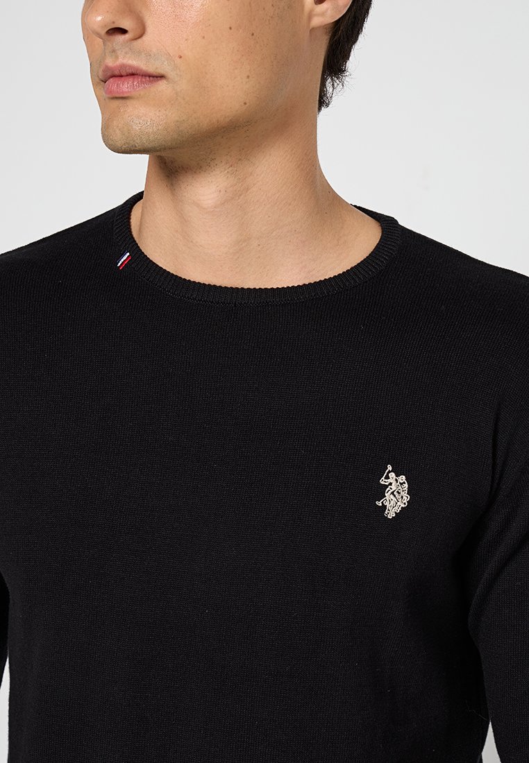 Schwarzer, gestrickter Pullover mit Rundhalsausschnitt, der ein kleines besticktes Emblem auf der Brust und einen dreifarbigen Akzent am Kragen aufweist.