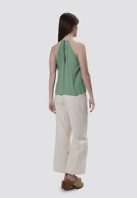 Top a halter verde con laccetti sul retro, abbinato a pantaloni larghi color crema. Il modello indossa zoccoli marroni con tacco quadra. Tessuto dalla texture liscia.