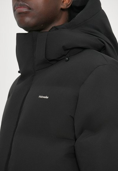 Black puffer jacket with a high collar, featuring a prominent logo on the chest, textured fabric, and button details on the hood.