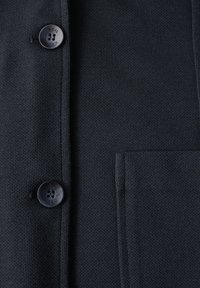 Cardigan blu scuro con un motivo a maglia testurizzato, dotato di due bottoni neri e una tasca sul lato sinistro.