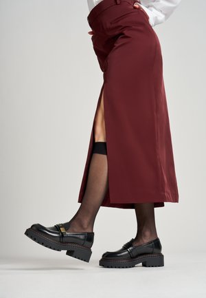 Falda larga burdeos con abertura lateral, combinada con unos mocasines negros gruesos y medias negras. Tela suave con un corte entallado y detalles en la cinturilla.