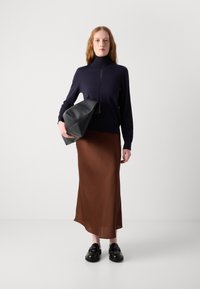Marine genser med høyt hals, brun satin skjørt med myk fall, og svarte slip-on sko. Modellen holder en svart lærveske.