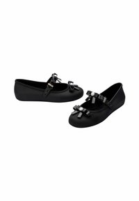 Zapatos planos negros de goma con punta redonda, que presentan un lazo negro brillante y un acento de perla en la correa. Textura suave y diseño minimalista.