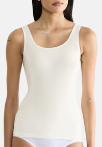 Top in crema con spalline larghe, scollo rotondo e texture liscia; progettato per una silhouette aderente, abbinato a slip bianchi.