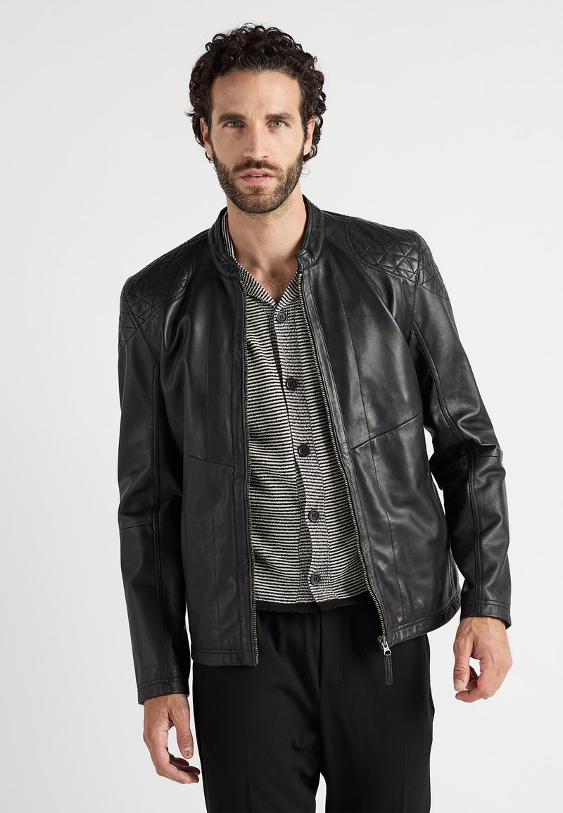 Zwarte leren jas met gequiltte schouderaccenten, staande kraag, rits aan de voorkant en slank ontwerp. Binnenkant toont een grijs gestreept shirt.