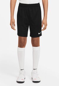 Schwarze Sportshorts mit einem elastischen Bund und einem weißen Nike-Logo. kombiniert mit weißen knielangen Socken und schwarzen Sportschuhen.