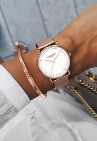 Montre avec bracelet en maille dorée rose et cadran blanc, ornée d'index et d'aiguilles dorées roses. Accompagnée d'un simple bracelet jonc en doré rose.