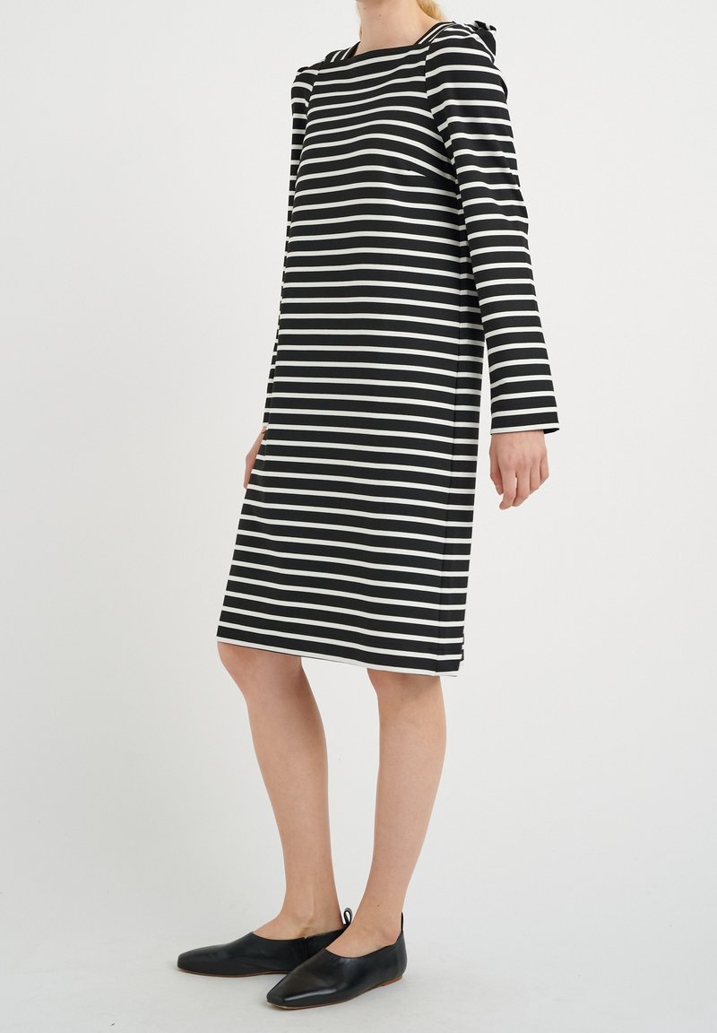 Robe à manches longues à rayures noires et blanches, coupe décontractée avec fentes latérales, associée à des chaussures plates noires. Texture de tissu lisse.