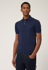 Marinblå polo t-shirt i strukturerad stickad kvalitet med krage, korta ärmar och tre-knapps knäppning, med en liten logotyp på bröstet.
