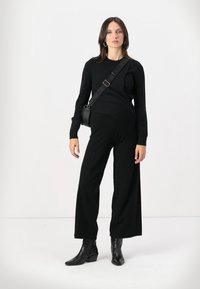 Black knit sweater with long sleeves, paired with wide-leg black pants. Black ankle boots and a small crossbody bag complete the outfit.