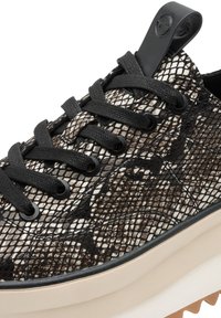 Primo piano di una sneaker con lacci neri, tomaia con motivo a serpente beige e nero e una sola spessa bianca con battistrada beige.