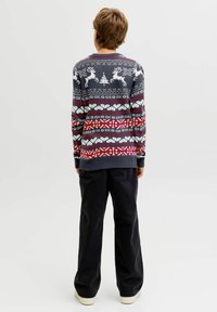 Tengerészkék kötött pulóver, amelyet a fair isle minta díszít, rénszarvasokkal és geometrikus mintákkal vörös, fehér és szürke színekben. Hosszú ujjak, bordázott mandzsetták.