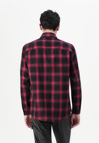 Camisa de manga larga en diseño de cuadros en negro y rojo. La tela es suave, con un cuello clásico y puños abotonados. Presenta un dobladillo curvado y un yugo trasero.