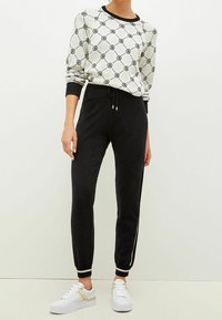 Weißes und schwarzes gemustertes Sweatshirt mit Rundhalsausschnitt, kombiniert mit schwarzen Jogginghosen mit elastischen Bündchen und seitlichen Streifen, getragen mit weißen Sneakers.