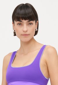 Μωβ αθλητικό σουτιέν με απλή υφή και φαρδύτερες τιράντες. Αντίθετες ραφές σε ανοιχτό μωβ τονίζουν τις άκρες. Απλός σχεδιασμός.