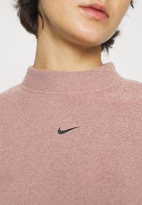 Rosa höghalsad sweatshirt i mjukt tyg, med en svart Nike-logotyp broderad på framsidan.