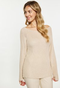 Vaalean beige pitkähihainen neulepaita, jossa on olkaimeton muotoilu, ribbaustekstuuri ja sivuhalkiot. Sileä kangas, jossa on hienovaraisia metallilankakoristeluja.