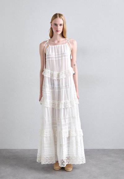 Robe maxi blanche avec des volants superposés, des dentelles et des bretelles réglables. Tissu léger avec des accents à motifs et un design fluide.