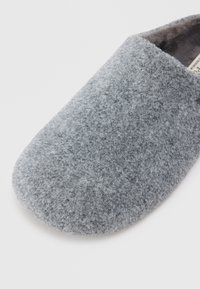 Chinelo de lã cinza com ponta arredondada, exterior de feltro texturizado e um interior macio. Sem hardware ou acabamentos visíveis.